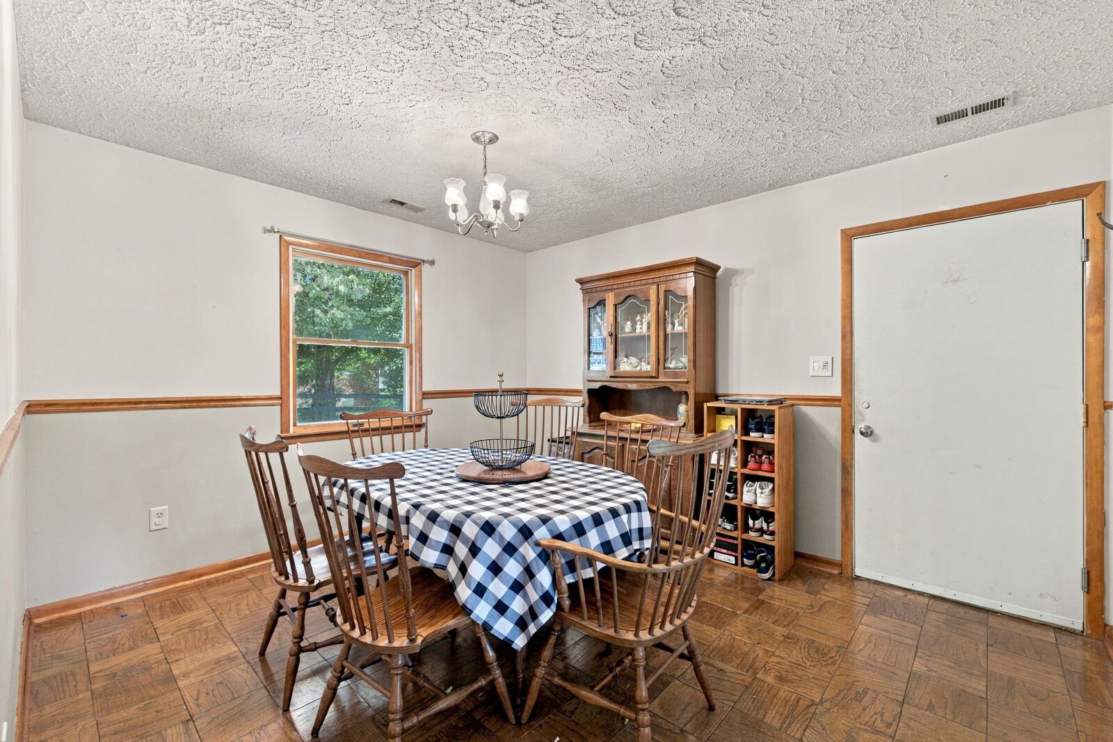 Dining room with a chandelier, a round table and chairs, wood chair rail, a side window and an exterior door.