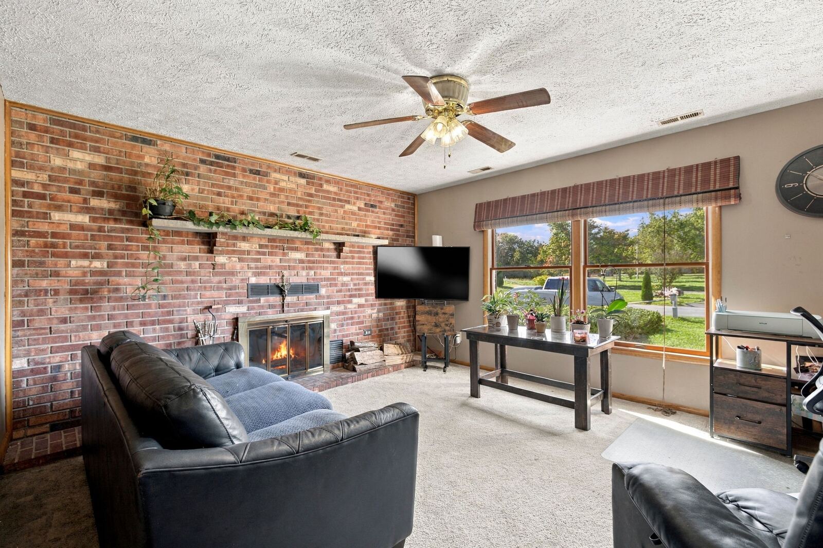 Family room with a full brick wall and fireplace, a ceiling fan, a large window and leather sofas.