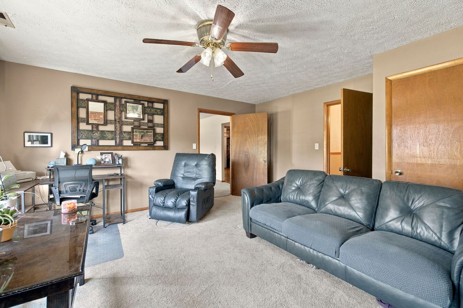 Family room with carpet, a leather sofa and recliner, a ceiling fan and doorways to the hall.