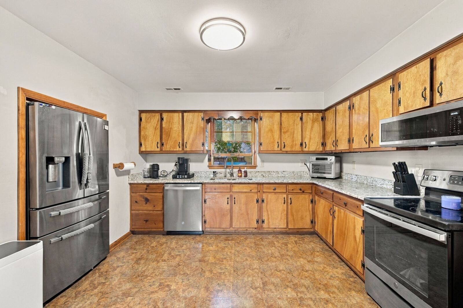 Kitchen with wood cabinets, a stainless French-door refrigerator, dishwasher, range and microwave, and a tile floor.