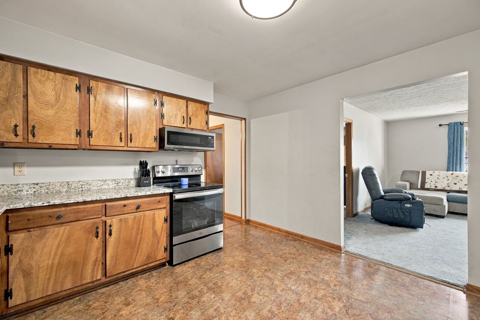 Kitchen with wood cabinets, light stone-look counters and a stainless range, opening to the living room.
