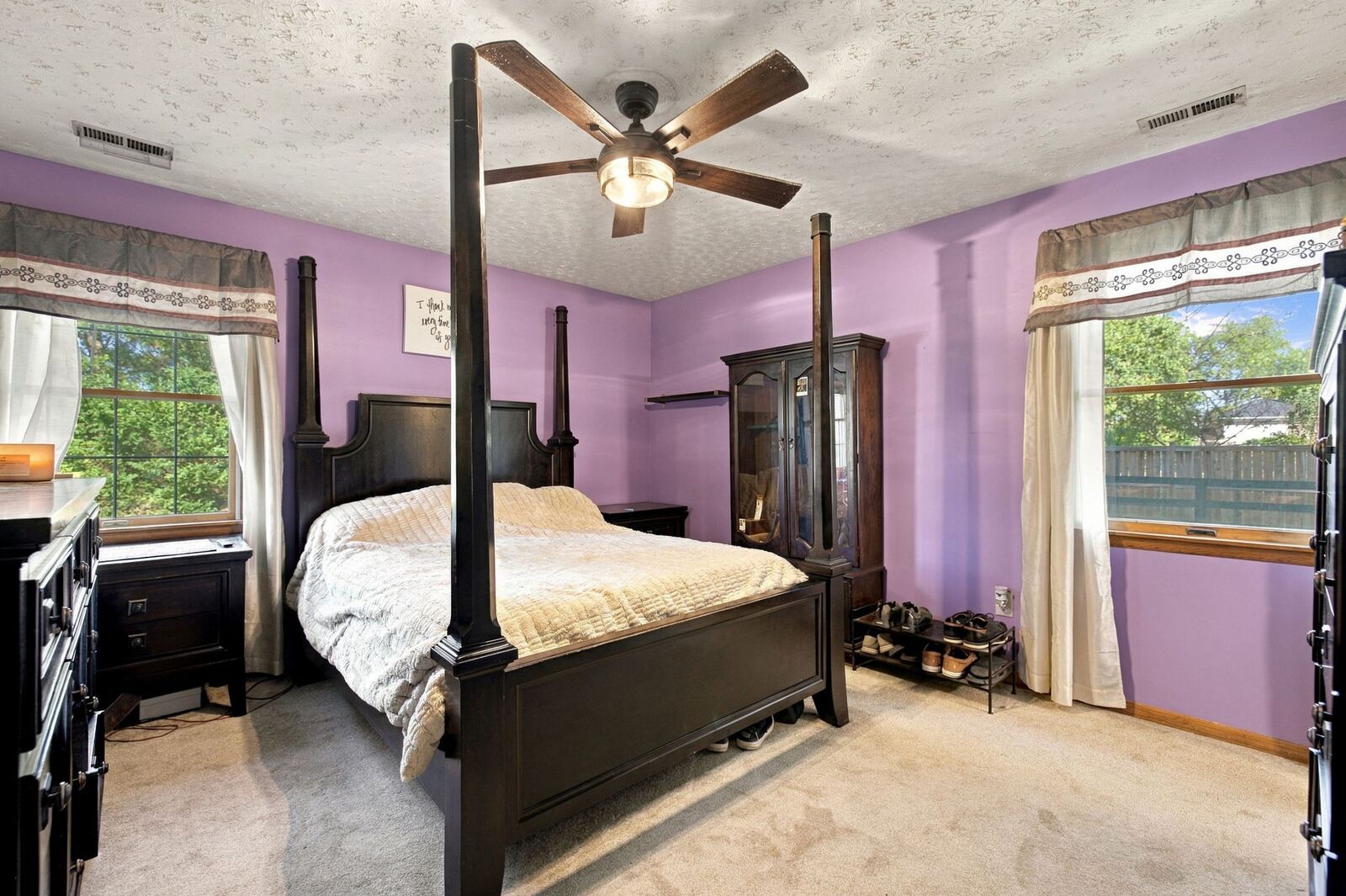 Primary bedroom with a four-poster bed, a ceiling fan, carpet and two windows.