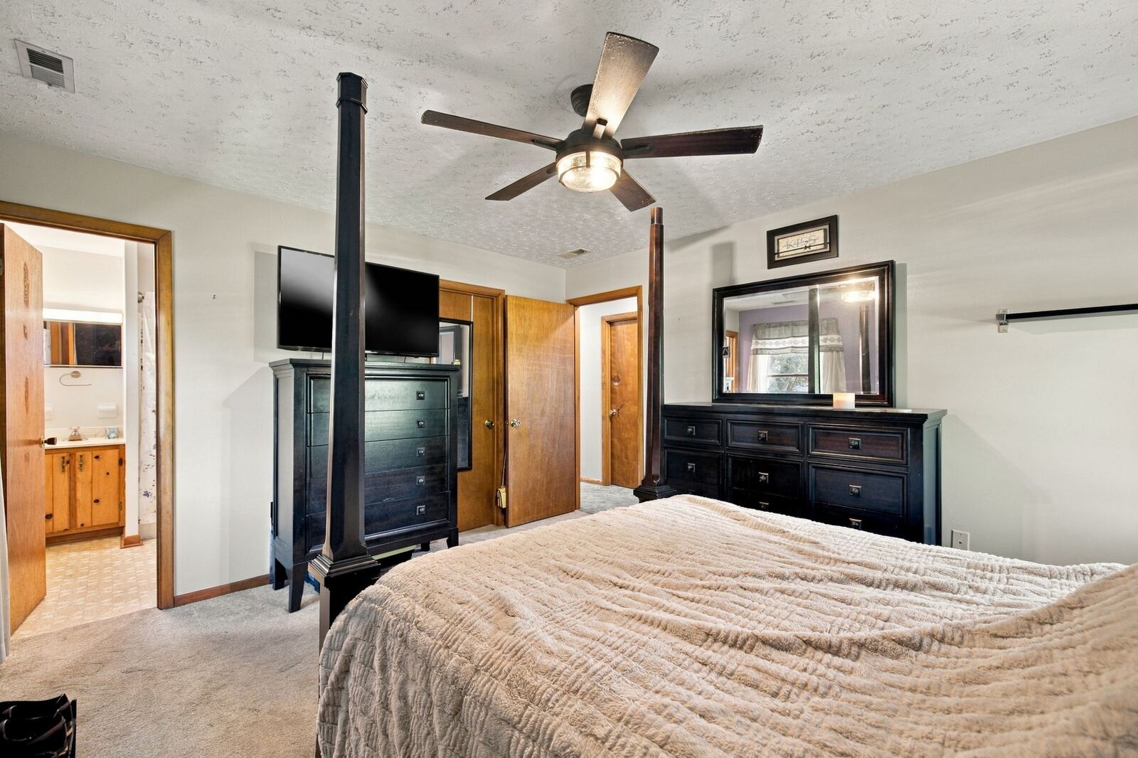 Primary bedroom with a dresser and mirror, a tall chest, a ceiling fan and two doorways.