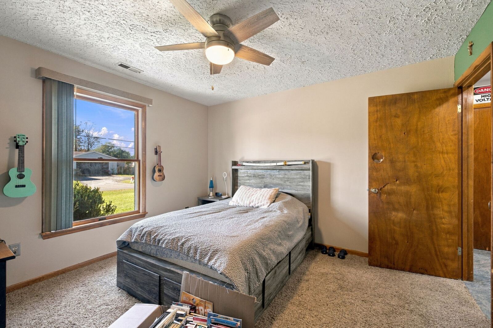 Bedroom with a ceiling fan, a bed with storage drawers, carpet, a window and a wood door.
