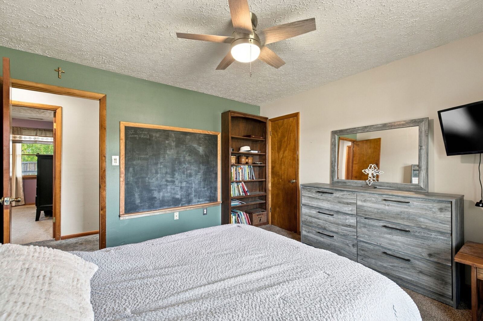 Bedroom with a gray dresser and mirror, a chalkboard panel, a bookshelf and a doorway.