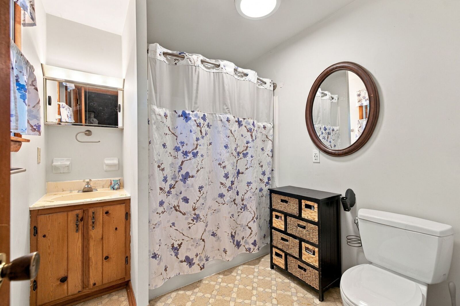 Primary bath with a wood vanity, a mirror, a toilet, a shower curtain and a small storage cabinet.