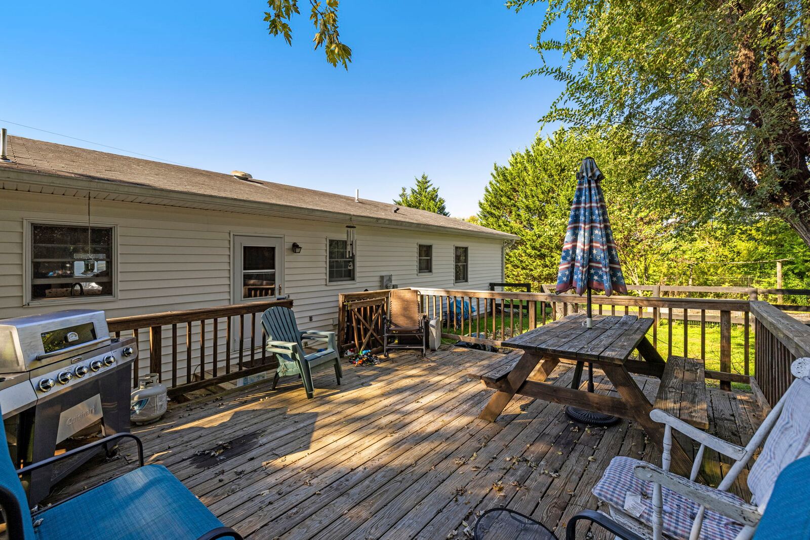 Rear deck along the back of the home with a grill, a table and a patio umbrella beside the siding.