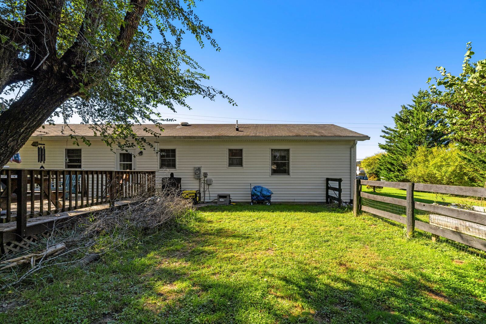 Rear of the home with the deck and siding, facing a wide grassy back yard under a blue sky.