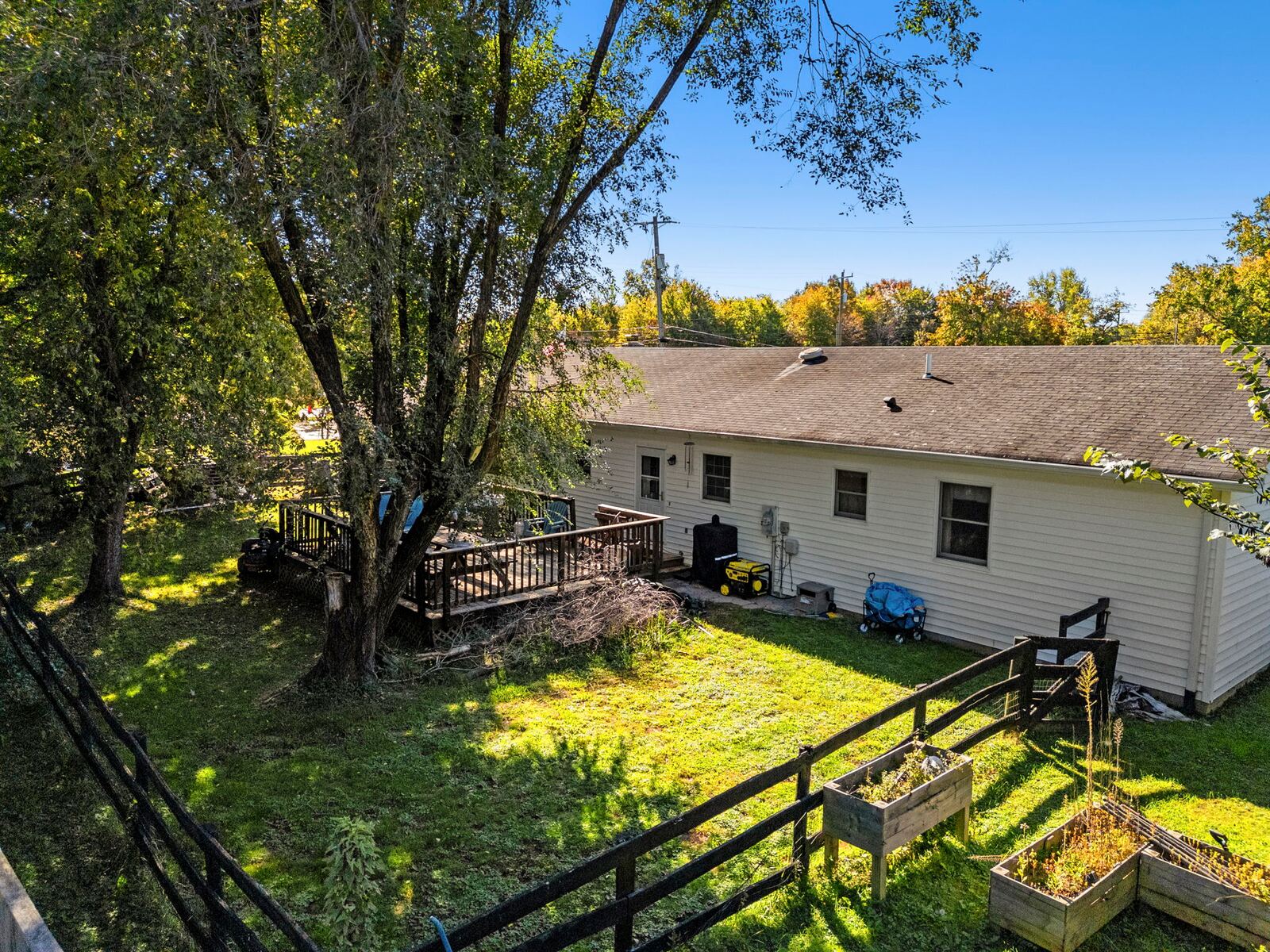 Aerial view of the back of the home, the deck, the fenced yard and large trees.